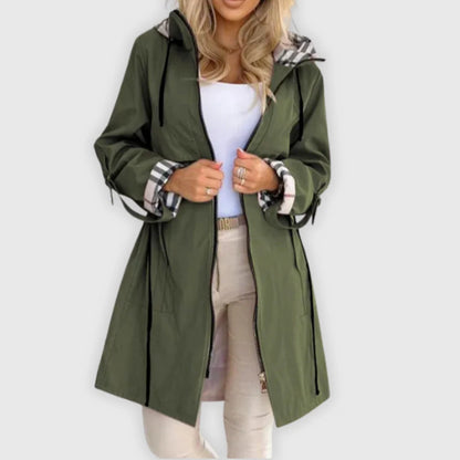 Woman wearing an olive green hooded coat with plaid lining and cuffs over a white top and light pants.