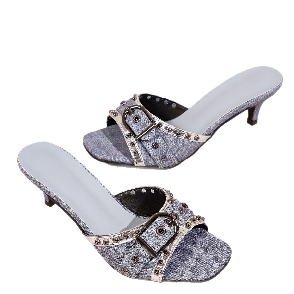 Pair of blue denim slide sandals featuring silver-toned buckles, studded trim, and kitten heels against a white background.