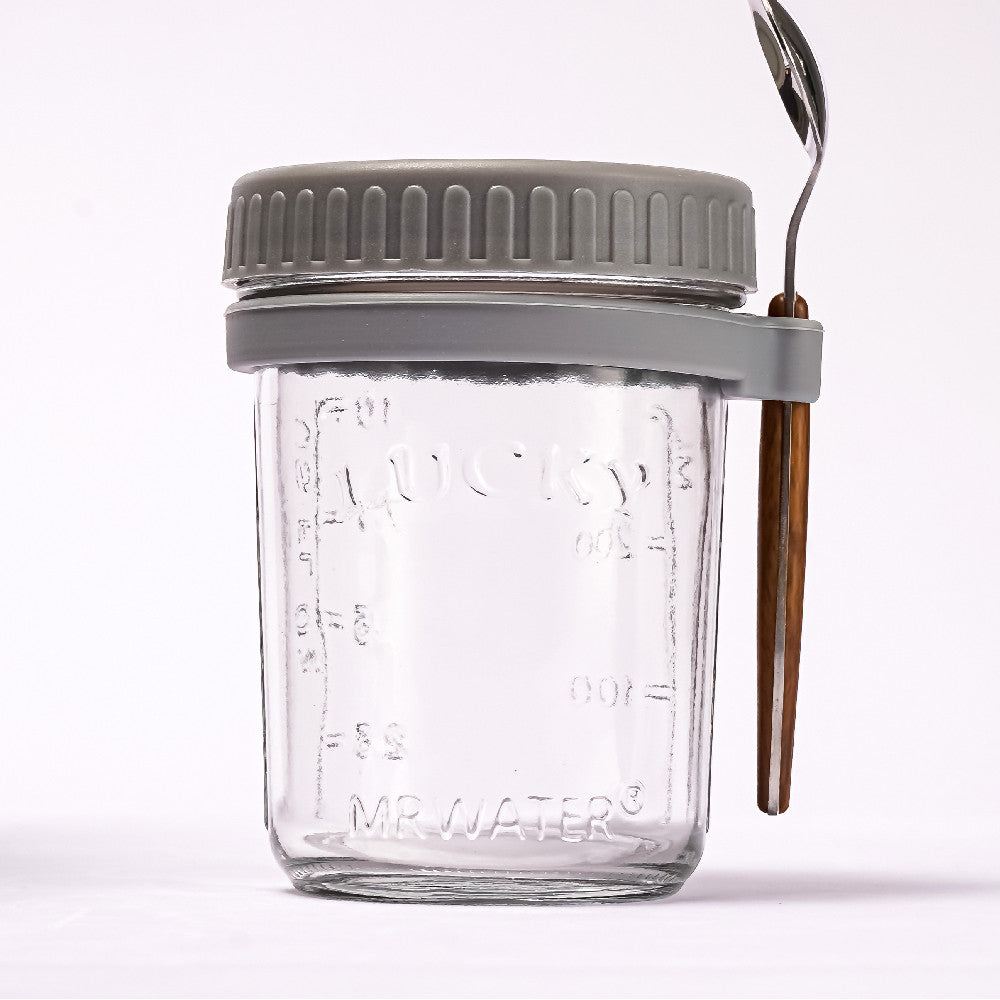 Glass overnight oats jar with a grey lid and ring holding a spoon with a wooden handle.