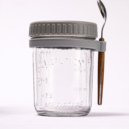 Glass overnight oats jar with a grey lid and ring holding a spoon with a wooden handle.
