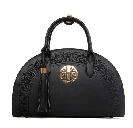 Black half-moon handbag with embossed pattern, gold medallion, and matching tassel.