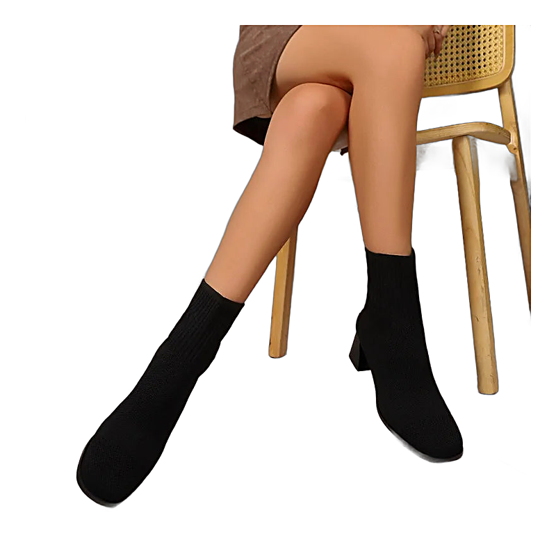 Black knitted sock ankle boots with square heels worn by a seated woman