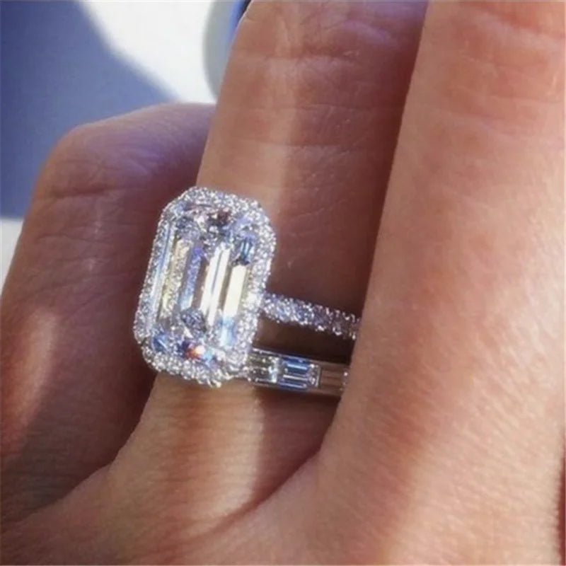 Two silver rings featuring a large emerald-cut cubic zirconia center stone, halo pave setting, and crystal accents.