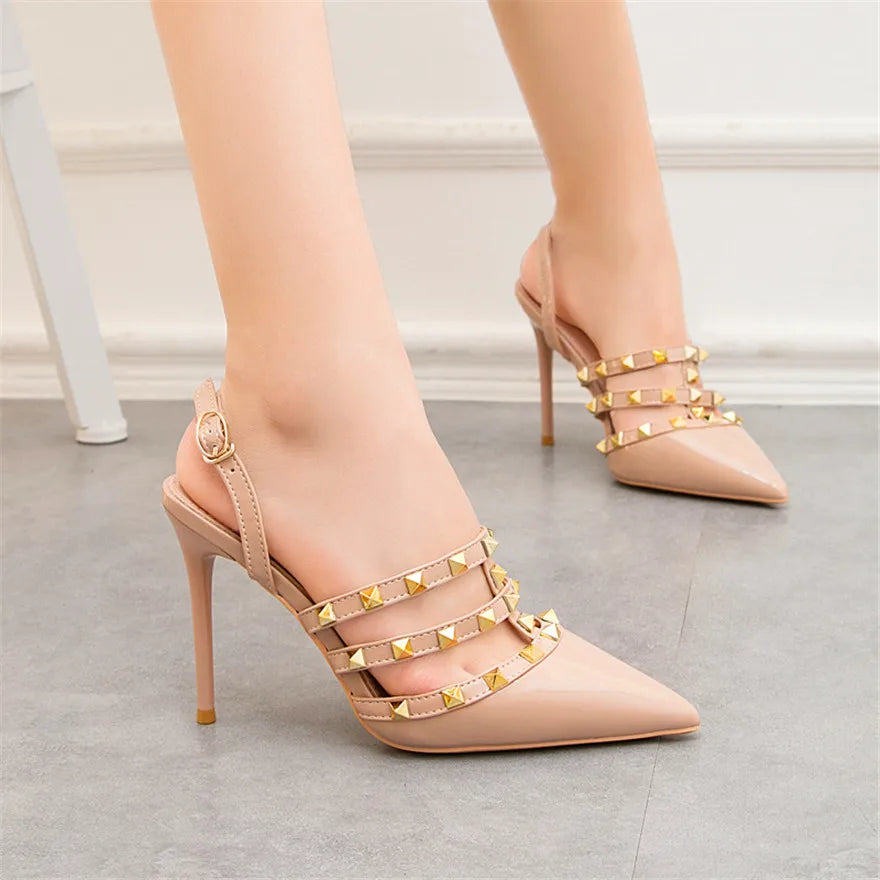 Beige patent leather ankle strap heels with gold rivet studs and stiletto heel for office wear.