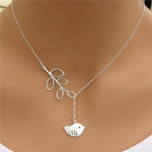 Silver-colored metal lariat necklace featuring a branch pendant with open leaves and a hanging bird pendant.