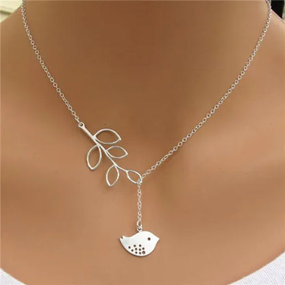Silver-colored metal lariat necklace featuring a branch pendant with open leaves and a hanging bird pendant.