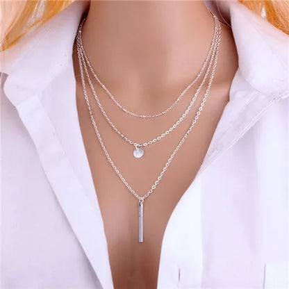 Silver-colored metal multilayer chain necklace with a small round coin pendant and a vertical bar pendant.