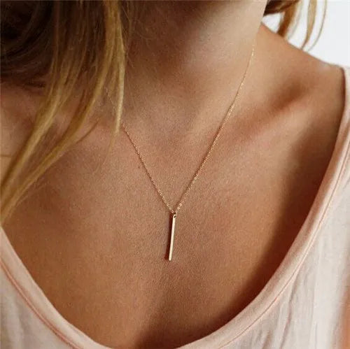 Gold-colored metal chain necklace featuring a slim vertical bar pendant worn around a woman's neck.