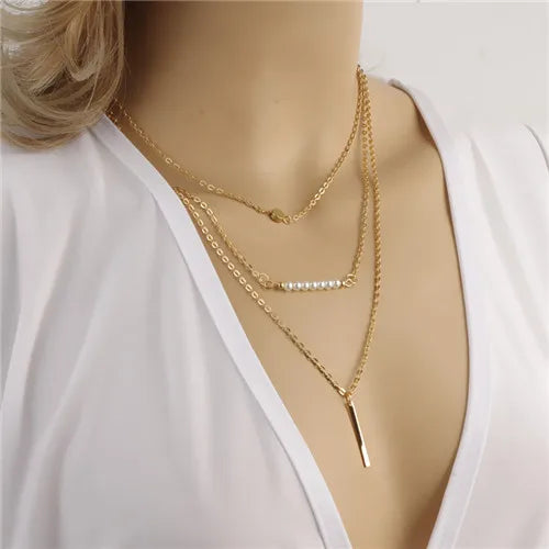 Gold-colored multilayer chain necklace featuring a beaded bar and a vertical bar pendant.