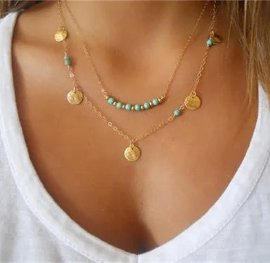 Gold-tone multilayer necklace featuring turquoise beads, hanging coin charms, and delicate chains.
