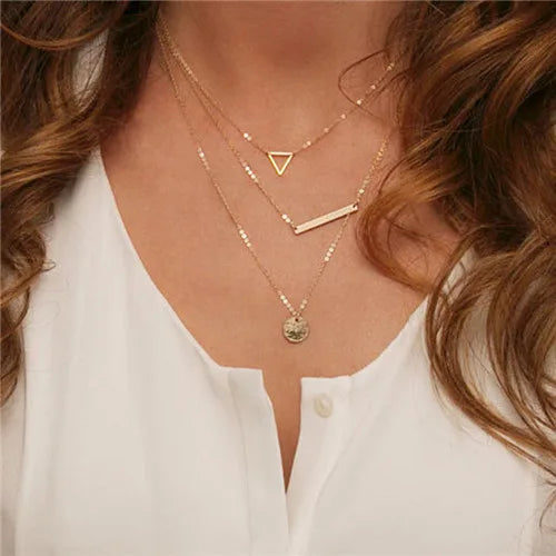 Gold-colored multilayer chain necklace featuring triangle, bar, and coin pendants.