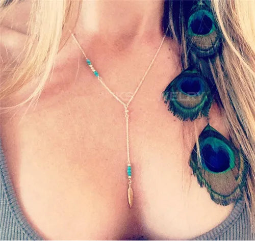 Gold lariat necklace with turquoise beads and a feather pendant, worn on a person.
