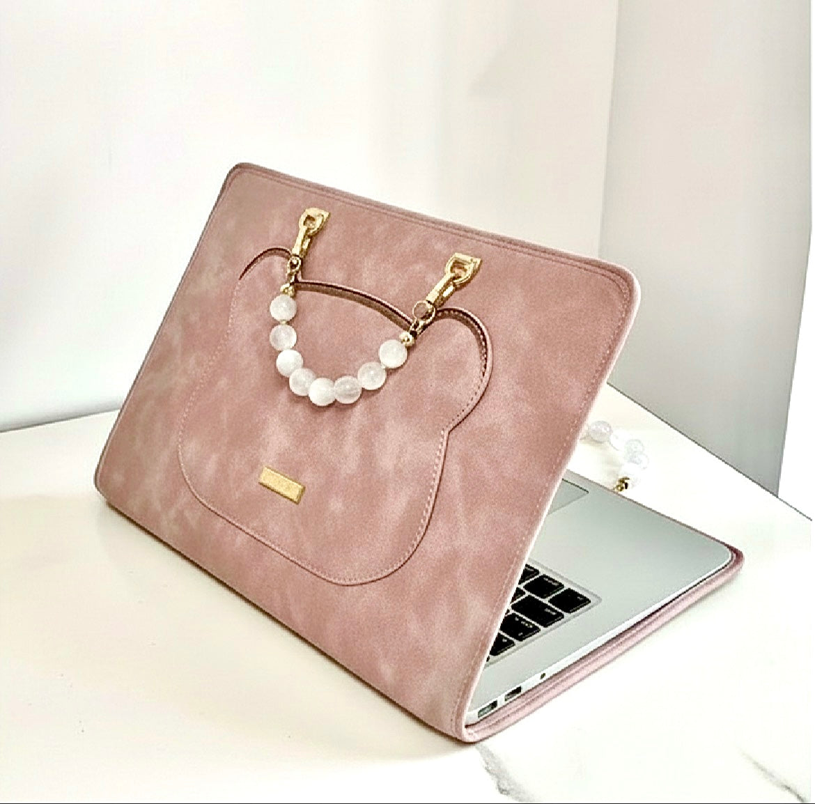 Pink suede laptop case with bear pocket, gold hardware, and pearl beaded handle on white surface.