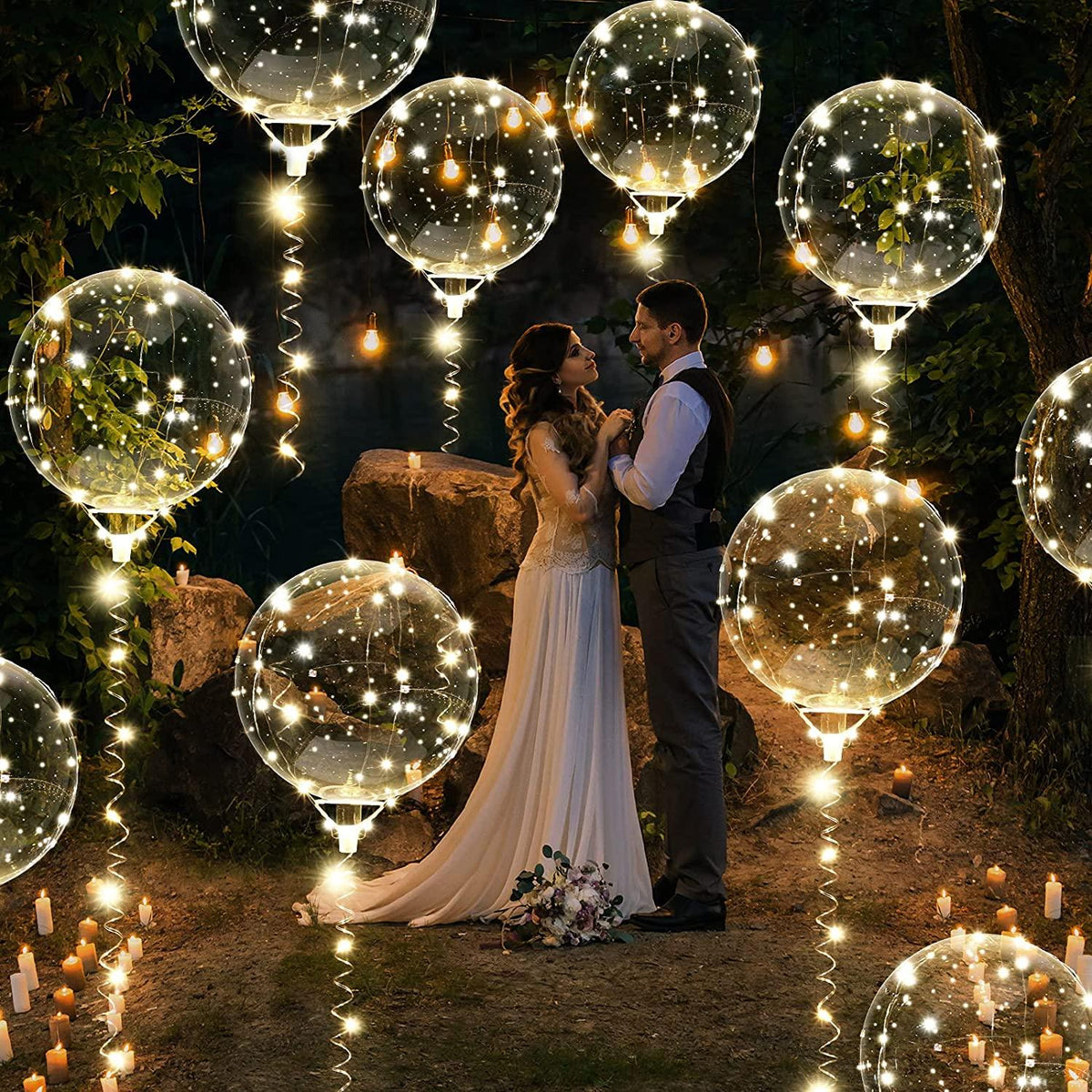 Clear round balloons wrapped with warm white LED string lights floating outdoors at night around a couple.