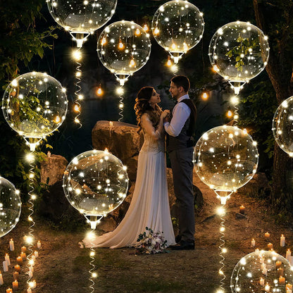 Clear round balloons wrapped with warm white LED string lights floating outdoors at night around a couple.