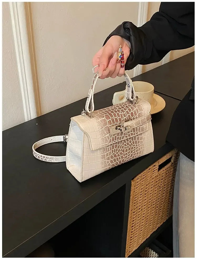 White faux leather structured diaper bag with crocodile texture, metal closure, and adjustable strap for carrying baby gear.