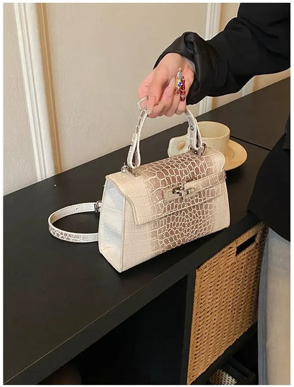 White faux leather structured diaper bag with crocodile texture, metal closure, and adjustable strap for carrying baby gear.