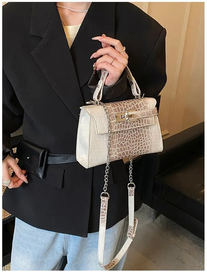 White faux leather crossbody diaper bag with crocodile texture, gold clasp, and adjustable strap for baby essentials.