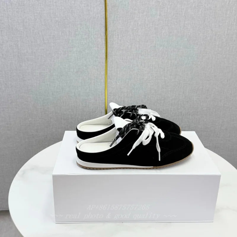 Black suede backless slip-on loafers with round toes, white laces, and flat white soles.
