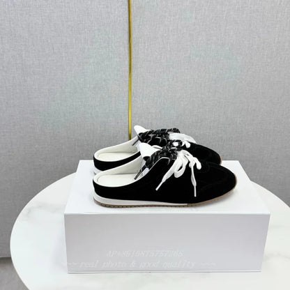 Black suede backless slip-on loafers with round toes, white laces, and flat white soles.