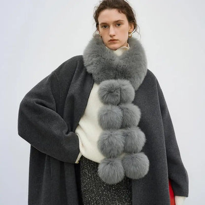 Gray long faux fox fur scarf with fluffy pom-pom details, worn around the neck.