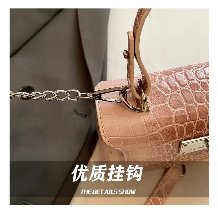 Pink faux leather diaper bag with crocodile texture, metal chain, and adjustable strap for carrying baby supplies.