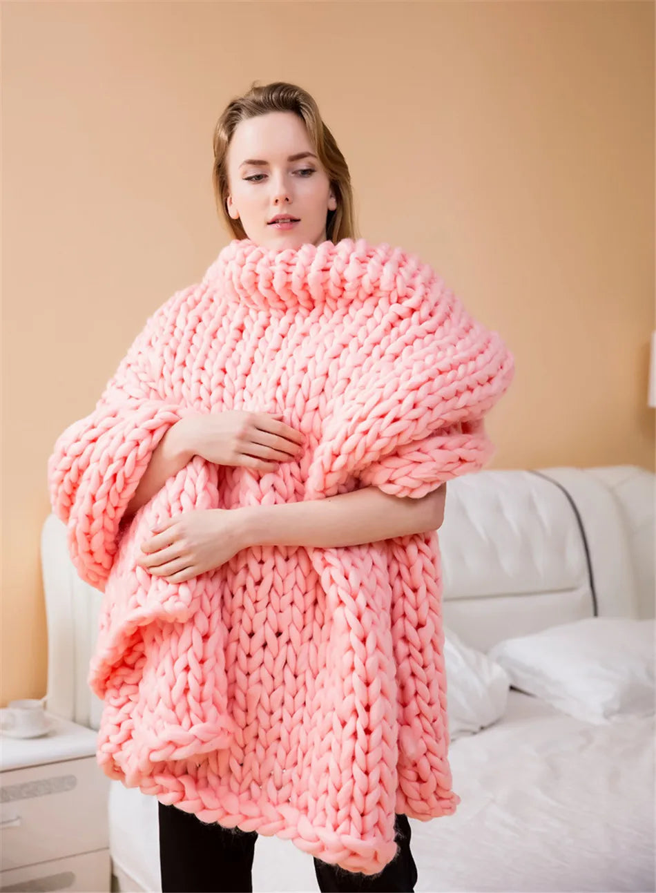 A woman wrapped in a chunky pink knit yarn roving blanket, styled as a cozy oversized cowl-neck sweater.