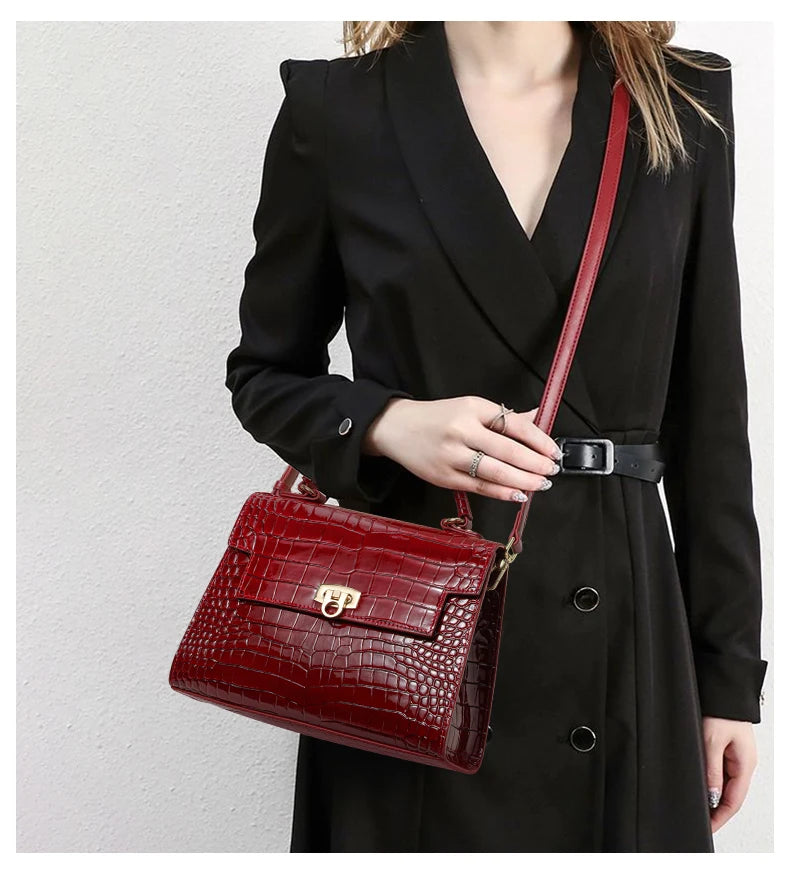 Glossy dark red leather crocodile-pattern handbag with gold clasp and matching crossbody strap worn by a woman.
