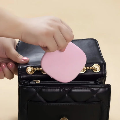 Round light pink LED makeup mirror with adjustable brightness for travel, being placed into a black quilted handbag.