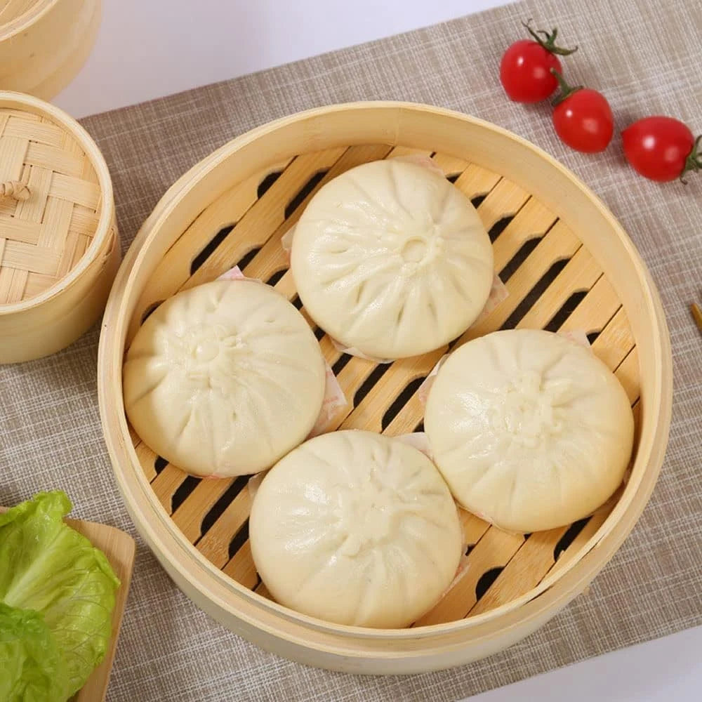 Natural bamboo steamer basket holding four white steamed buns.
