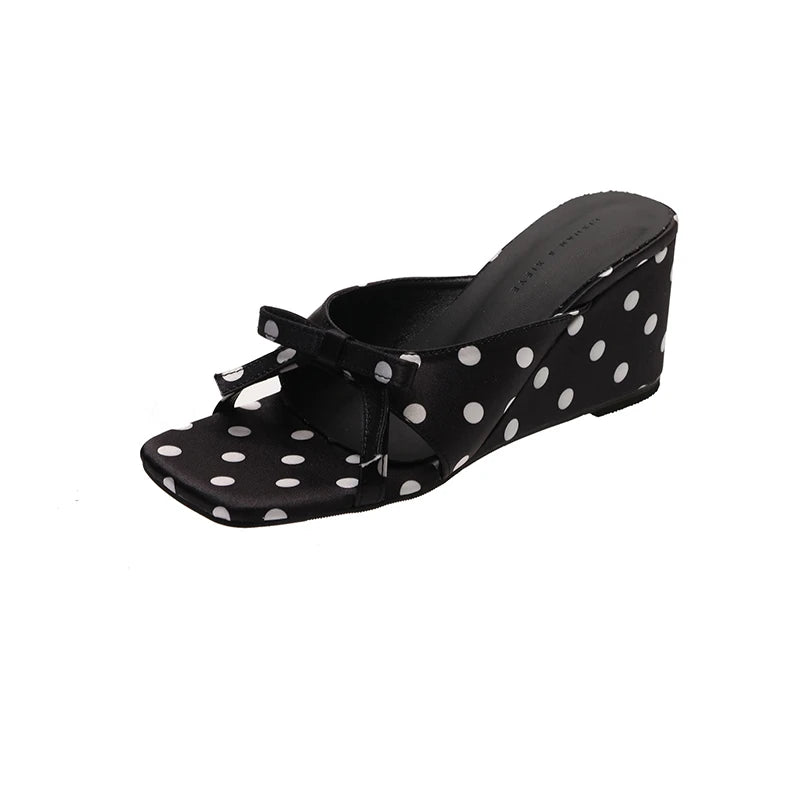 Black polka dot wedge sandals with a front bow detail and slip-on design for casual wear.