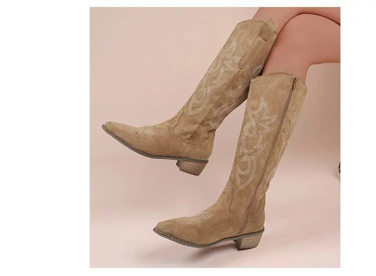 Tan suede knee-high Western cowboy boots with white stitch embroidery and block heels.