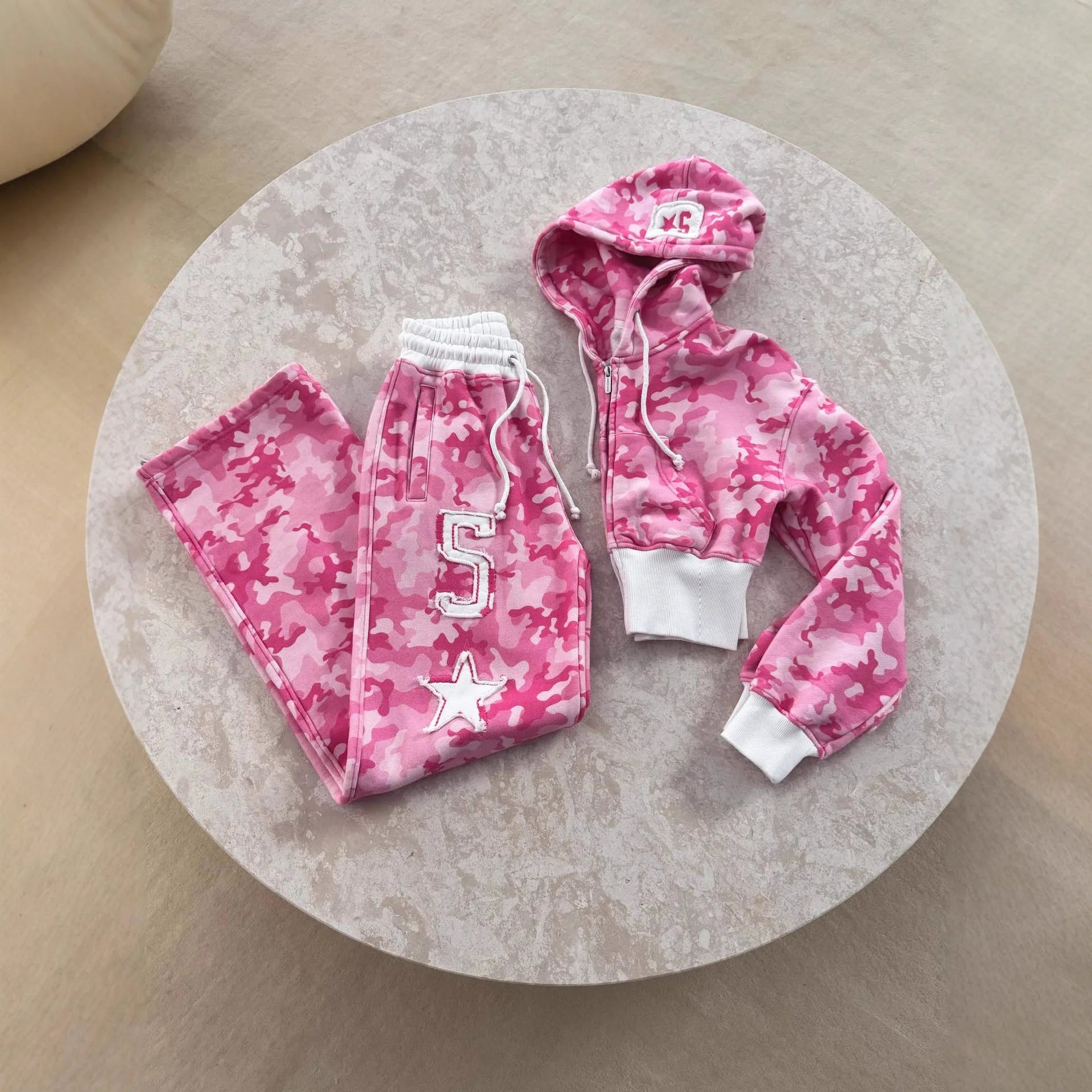 Pink camo oversized sports set with white letter and star patches, drawstring waist, and zip hoodie for active wear.