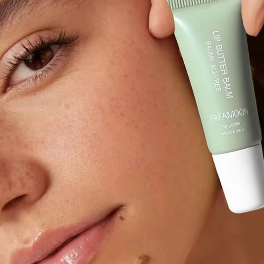 Close-up of a person holding a light green lip butter balm squeeze tube near their cheek.