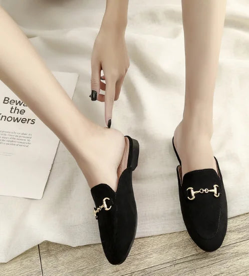 Black suede slip-on mules with a gold metal chain detail for comfortable outdoor wear.
