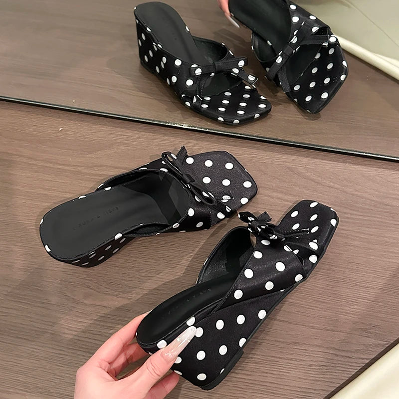 Black and white polka dot wedge sandals featuring a bow detail and cushioned insole for casual wear.