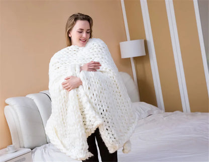 A woman holding a thick, chunky white knitted yarn roving blanket in a bedroom.