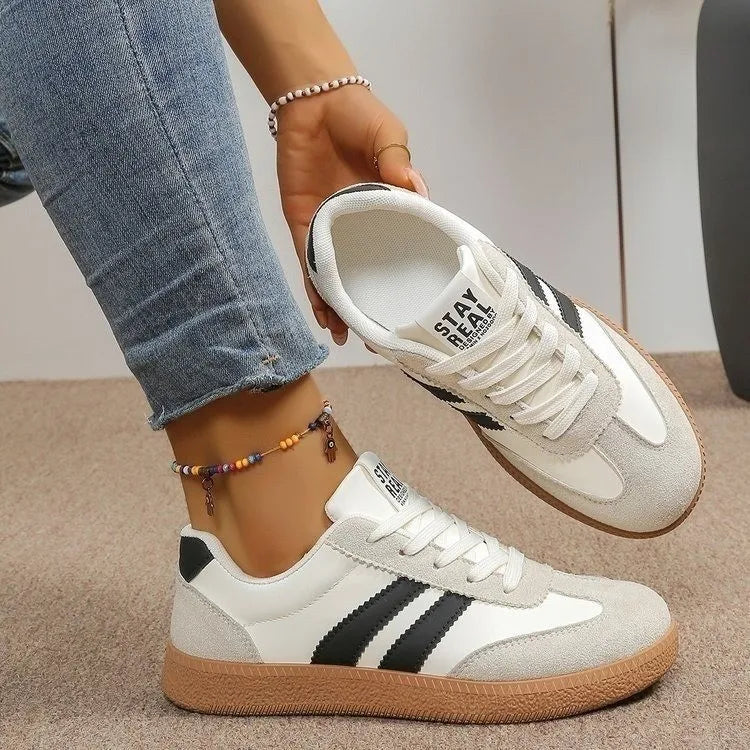 White leather sneakers with black stripes and tan soles, styled as slip-on shoes for casual everyday wear.