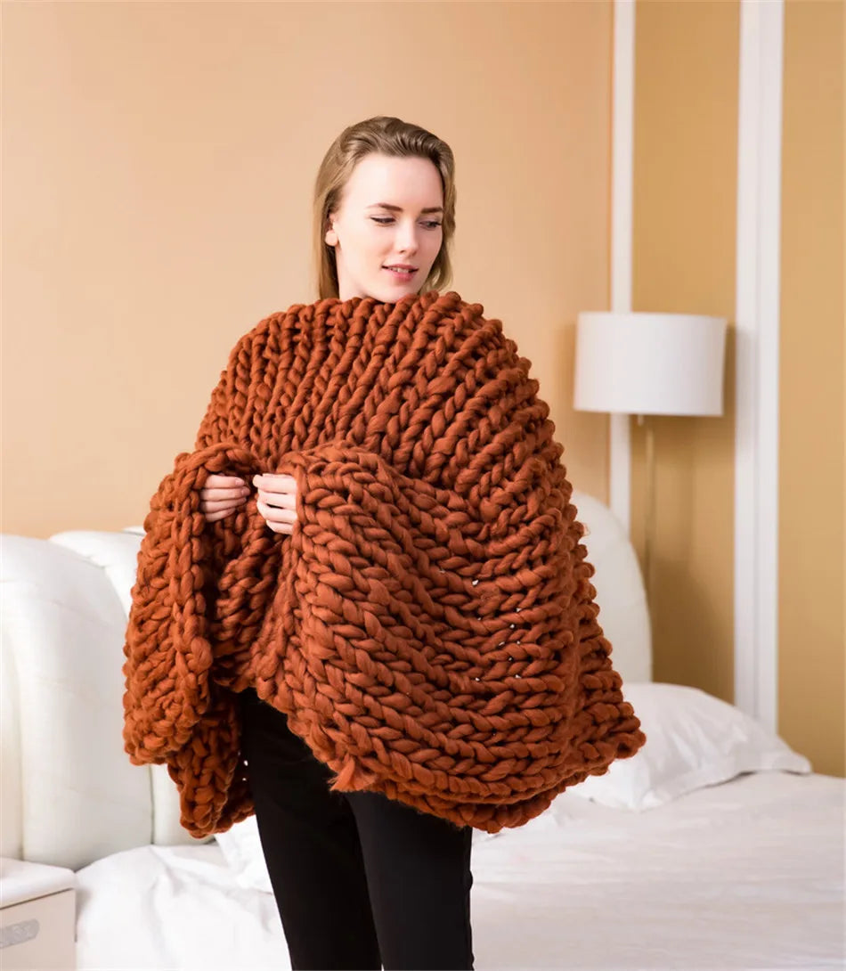 A woman draped in a rust-orange, chunky hand-knitted roving blanket made of thick yarn.