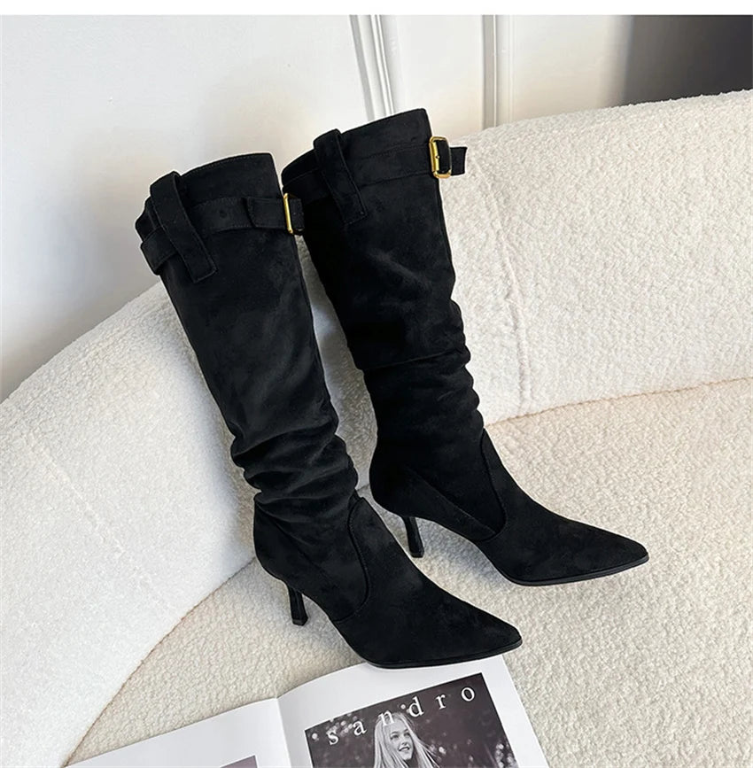 Black suede pointed-toe slouchy knee-high boots with thin heels and gold buckle straps.