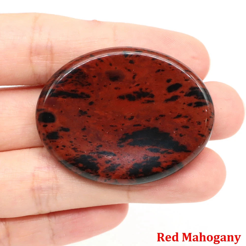 Polished oval red and black mahogany obsidian palm stone for home decor meditation sessions held in a hand.