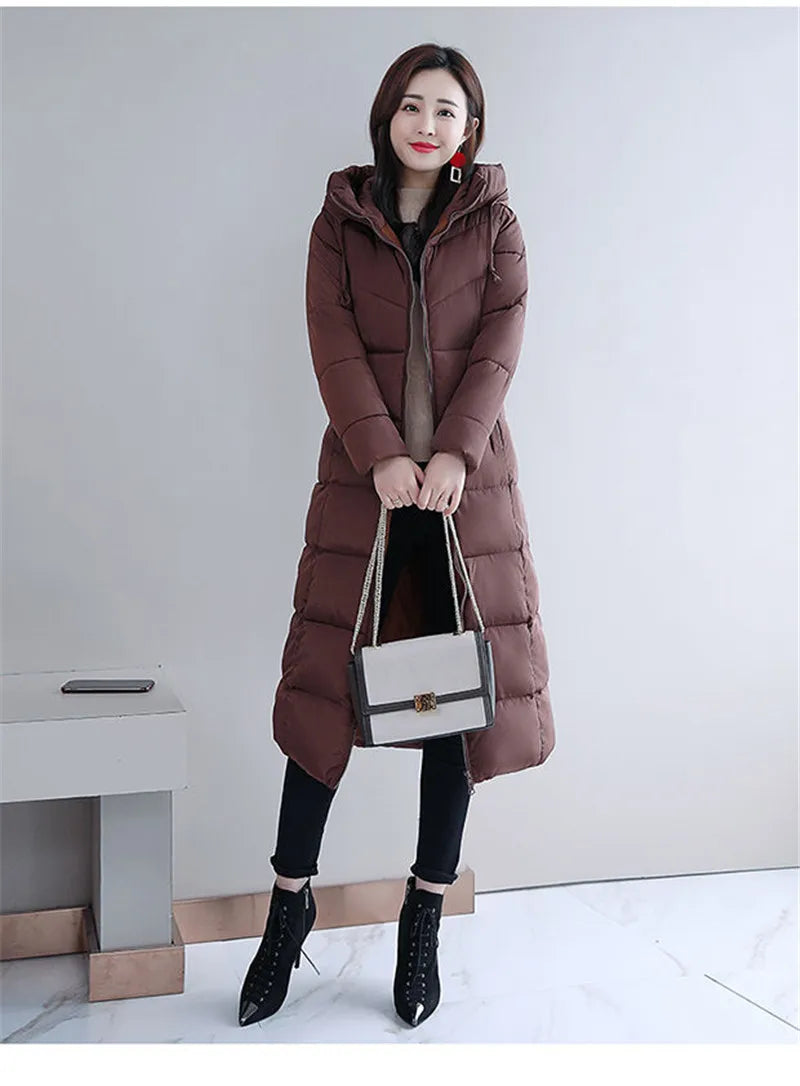 A woman wearing a long, quilted brown puffer parka with a hood, black pants, and boots.
