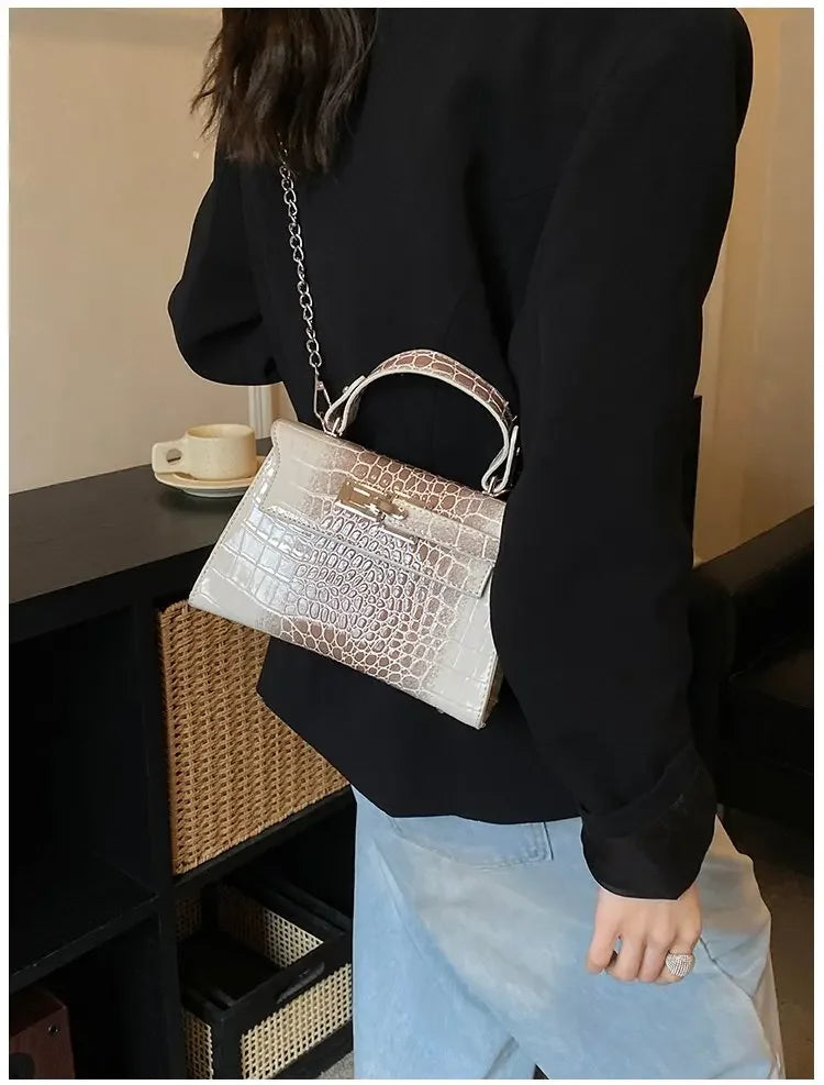 Beige croc-embossed faux leather structured diaper bag satchel with top handle for carrying baby essentials.