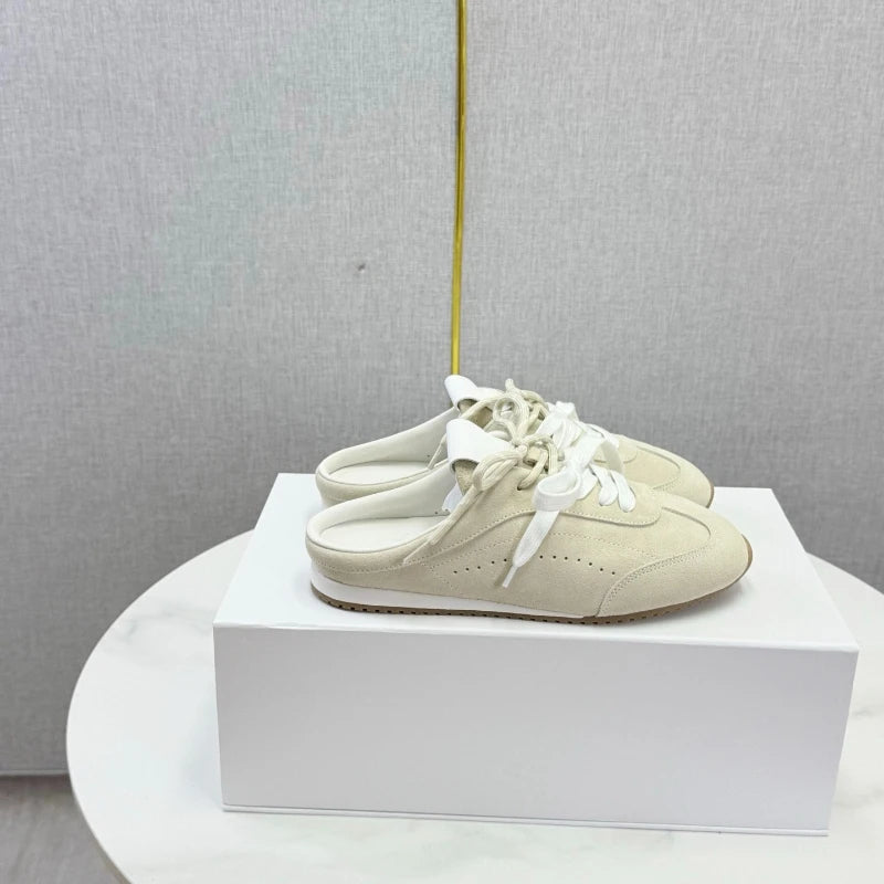 Beige suede slip-on casual shoes with round toes, white laces, and open backs, resting on a white box.