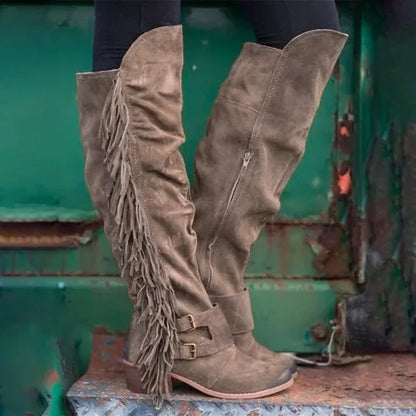 Taupe suede over-the-knee boots with long fringe, double ankle buckle straps, and thick heels.