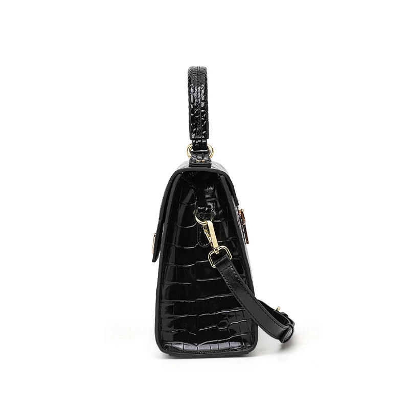 Black glossy crocodile-pattern leather handbag with top handle, gold hardware, and detachable shoulder strap.