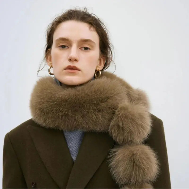 Brown faux fox fur scarf with plush pom-poms worn around the neck of a person in a dark coat.