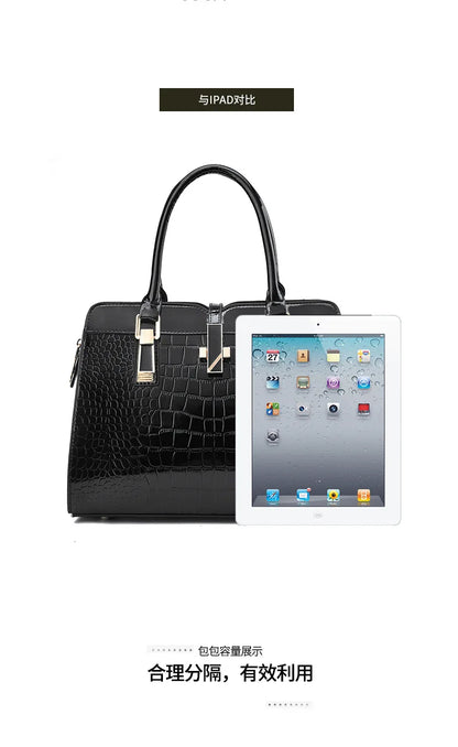 Black crocodile-pattern leather handbag with dual top handles, gold hardware, and a tablet shown for scale.