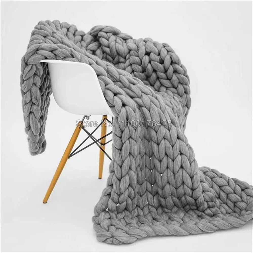 Grey chunky knit throw blanket draped over a modern white chair with wooden legs.