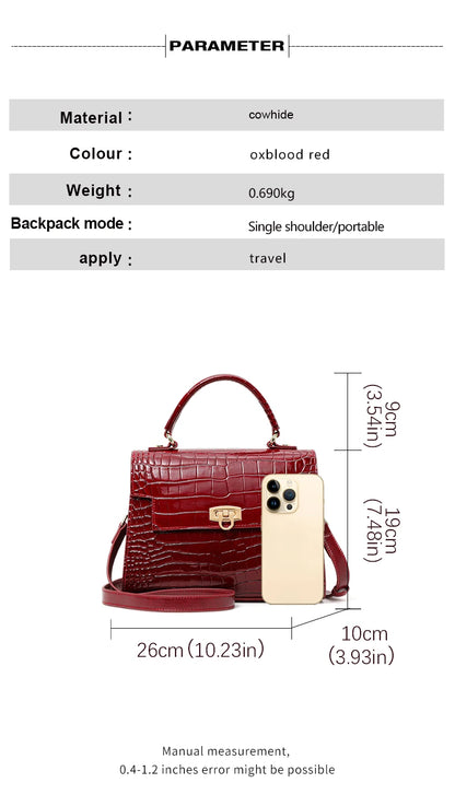 Oxblood red cowhide handbag with crocodile pattern, top handle, flap closure, and a gold clasp, shown with a phone for scale.